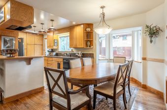 A warm and inviting dining area with a polished wooden oval table and comfortable seating, adjacent to a kitchen with light wood cabinetry and modern appliances.