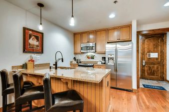 A kitchen with stainless steel appliances, wood cabinets, and a breakfast bar with two stools.