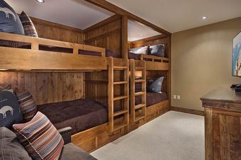A cozy bunk room at Buffalo Pass One Steamboat Place 409 features custom-built wooden bunk beds with comfortable bedding and colorful throw pillows, and a large flat-screen TV.
