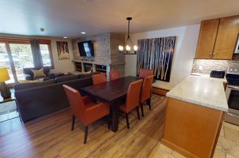 Dining area with a large wood table and chairs, and a living room with a couch and fireplace.