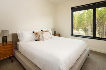 The spacious bedroom in Moonlight Basin 221 Lakelodge features a plush king bed, with white linens and decorative pillows, and a large window offering views of the surrounding forest.