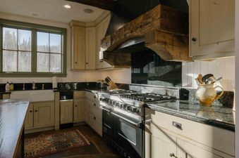 The kitchen at Elk Lake Lodge features light-colored cabinetry, dark countertops, a large stainless steel range, and a sink beneath windows.