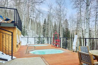 The private deck at Top of the Village Summit 103 features two hot tubs and an outdoor dining area, surrounded by snowy Aspen trees.