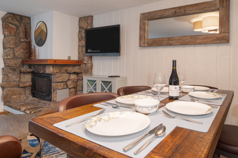 A close-up view of the set dining table in Beaver Village 1714, featuring plates, cutlery, glasses, and a bottle of wine, all ready for a meal.
