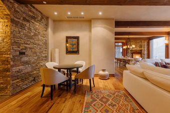 A spacious open-concept living area with a dining nook, a large stone fireplace, comfortable sofas, and a view of the outdoors.