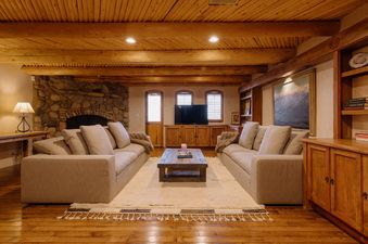 The Hang Glider Hideout's living area is furnished with two facing sofas on a cream rug, centered around a wooden coffee table, all beneath a rustic wood-beamed ceiling.