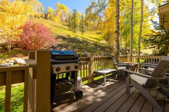 The deck at Stone Creek Chalet at The Aspens features a BBQ grill and Adirondack chairs.