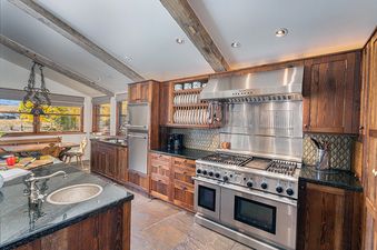 A kitchen with stainless steel appliances, wood cabinets, and a view of a field from the window.