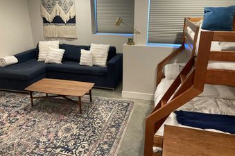 The living area of the Mountain Modern Duplex features a blue sectional couch, a wooden coffee table, and a patterned rug, with a bunk bed visible on the right.