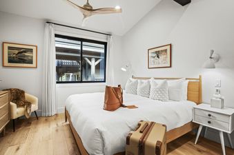 A bright and airy bedroom in Black Bear 404 with a wooden bed frame, white bedding, decorative pillows, a nightstand, and a large window with exterior views.