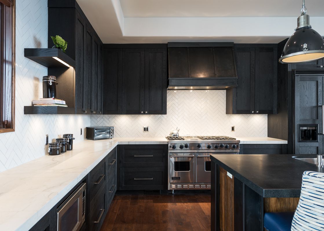 A modern kitchen at Silver Star 40 with dark wood cabinetry, white marble countertops, a herringbone backsplash, and stainless steel appliances.