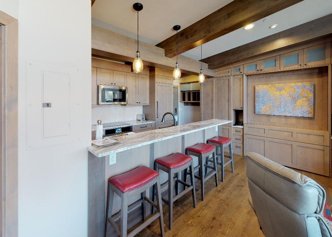 Kitchen with bar seating, a large living room, and an art piece above a fireplace.