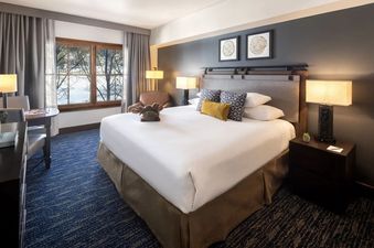 A cozy bedroom with a king bed, warm lighting, and a window view of snow-covered trees at the Teton Mountain Lodge and Spa One Bedroom Suite.
