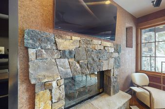The fireplace in Settlers Lodge 104 is made of natural stone and has a glass door. There is a large flat screen TV mounted above the fireplace.