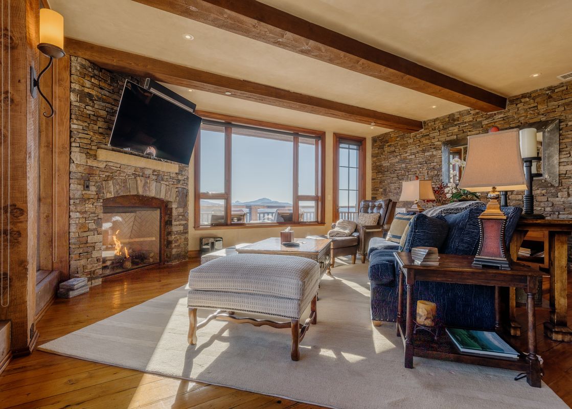 Luxurious living room in The Developers Residence at See Forever with stone fireplace, comfortable seating, and scenic mountain views.