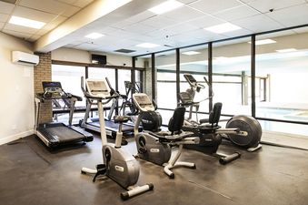 A bright and spacious gym at Resort Plaza 5043 with various exercise machines, large windows, and a view of an indoor pool.