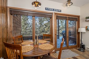 A cozy dining area with a wooden table, chairs, and large windows offering a view of snow-covered trees and mountains.