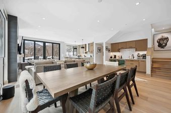 An expansive open-concept living area in One Riverfront Townhome 05, featuring a large dining table with woven chairs, a comfortable living room with mountain views, and a modern kitchen with a wet bar.