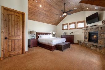 A spacious master bedroom at Snowtop Manor with a king bed, wooden vaulted ceiling, fireplace, and flat-screen TV.