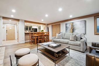 An inviting open-concept living and dining area with a grey sofa, wooden coffee table, and a wooden dining set connected to a kitchen.