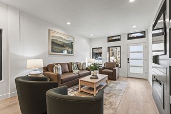 A living room with a brown leather sofa, a coffee table, two armchairs, and a fireplace.