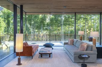 A living room with a large window overlooking a forest, a couch, and a coffee table.