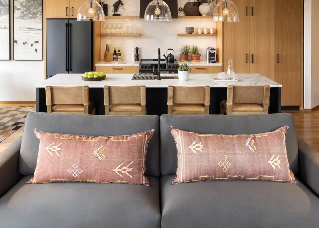 A wide shot of the open concept living area in The Sylvan Lodge Four Bedroom Penthouse, showing the kitchen, dining room, and lounge area, featuring modern furnishings and large windows with natural views.