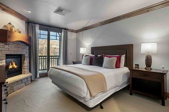 A cozy bedroom with a large bed, fireplace, and a balcony showcasing a scenic autumn mountain view at Silver Strike Lodge 305.