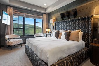 A luxurious bedroom at Flagstaff 507 with a patterned king-sized bed, bison accent pillows, elegant lamps, and a large window overlooking green mountains.