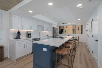 The modern white and blue kitchen features a spacious island with seating, white cabinets, and contemporary appliances under bright recessed lighting.