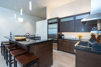 A modern kitchen with a stainless steel refrigerator, a gas stove, a dark wood island with a breakfast bar, and a light wood floor.