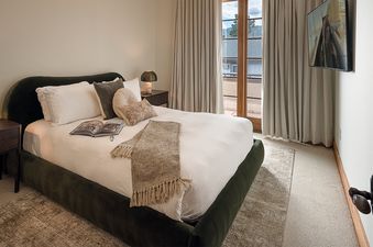 A modern and cozy bedroom with a queen bed, green velvet frame, balcony doors, and a wall-mounted TV.