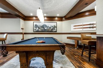 A sophisticated games room at Arrowleaf Lodge 311 features a billiard table, elegant decor, and comfortable seating, all illuminated by a modern chandelier.