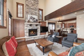 The grand living area of 751 Mountain Terrace features a stunning stone fireplace, comfortable seating, and an open-concept design flowing into the kitchen and dining areas.