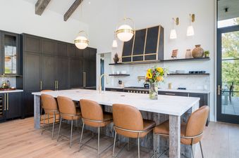 A modern kitchen at Big Wood River Retreat with dark wood cabinets, a large marble island with leather bar stools, and a view of an outdoor patio.
