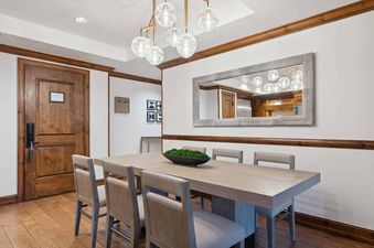 A modern dining room in The Aspen 12B featuring a wooden dining table, a large mirror, and a contemporary glass globe chandelier.
