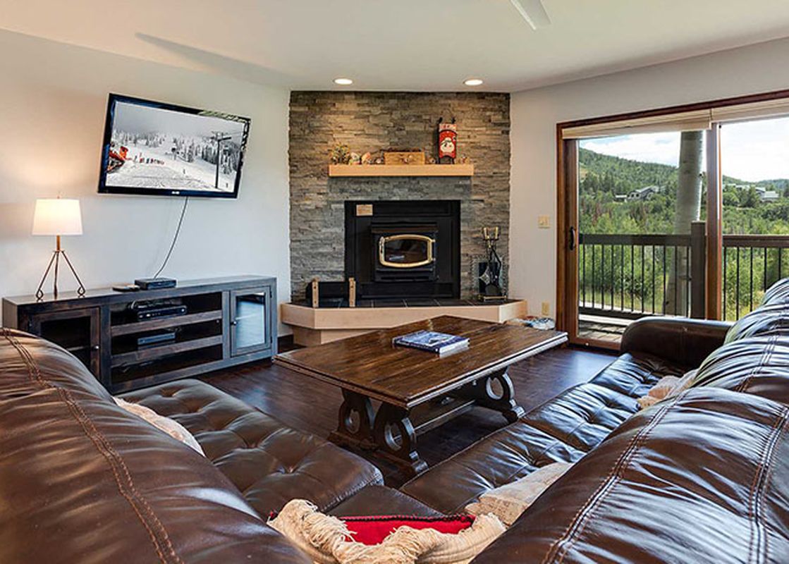 The living room of Ranch at Steamboat RA309 features brown leather couches, a fireplace, and a flat-screen TV, with a view of mountains from the balcony.