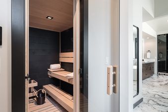 A modern sauna features light wooden benches and dark paneling, with a digital control panel on the adjacent wall.