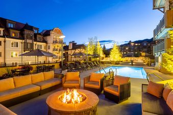 An outdoor area with a fire pit, couches, chairs, and a swimming pool is brightly lit at dusk.