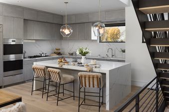A modern kitchen at Hidden Hollow 304 with gray cabinetry, white marble countertops, stainless steel appliances, and a kitchen island with bar stools.