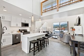 A modern kitchen and open-concept living area with white cabinetry, a kitchen island with seating, and a living room with mountain views, providing an alt text description of the space.