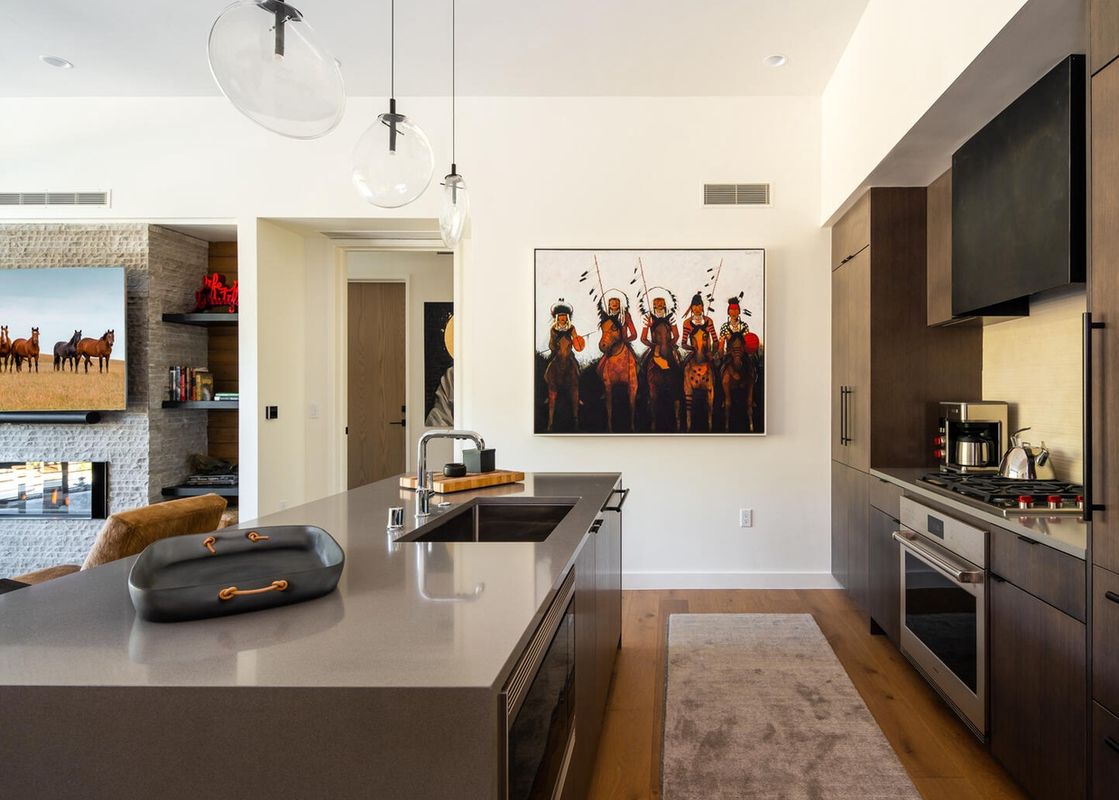 The kitchen at Moonlight Basin 215 Lakelodge features a stainless steel oven, a gas stovetop, modern cabinetry, and a large, expansive island with a sink and hanging pendant lights.