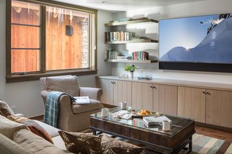 A cozy living room at Four Pines 102 features a comfortable sofa and armchair, a coffee table with snacks, built-in shelves with books, and a large TV.