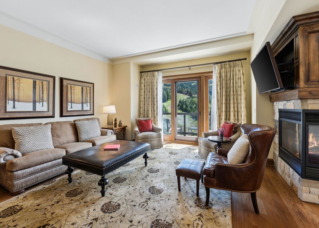 A lavish living room at the St Regis Madison Residence, featuring a cozy fireplace, comfortable seating, and a balcony with scenic mountain views.
