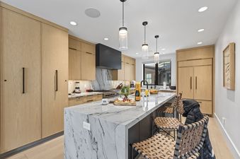 The modern kitchen at Abode at Hollow Mountain features light wood cabinets, a marble island with barstool seating, and stainless steel appliances.