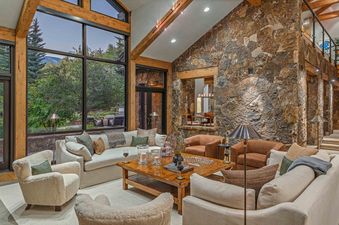A large living room with a stone fireplace, a large sectional sofa, and a coffee table with glasses of wine.