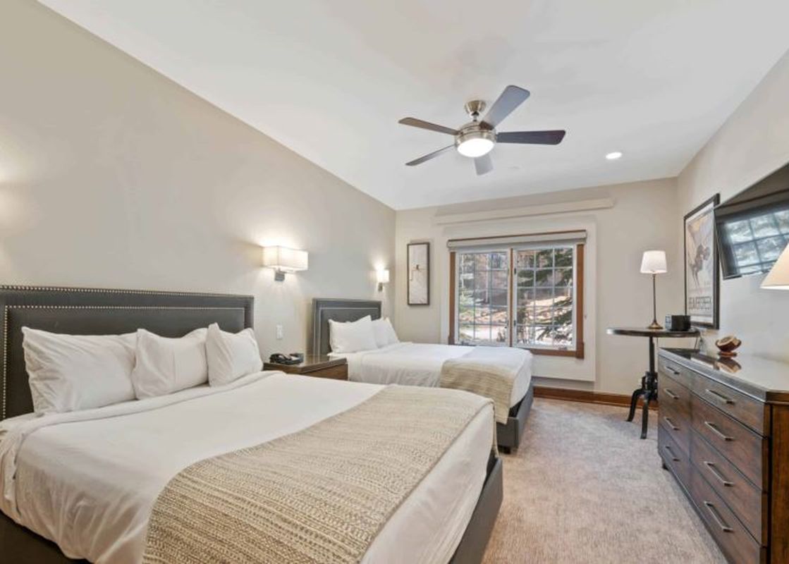 A hotel bedroom with a king-sized bed and a queen bed, a dresser with a TV, and a window with an outdoor view.