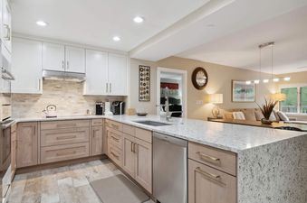 A modern kitchen with light wood cabinets, white countertops, and stainless steel appliances.