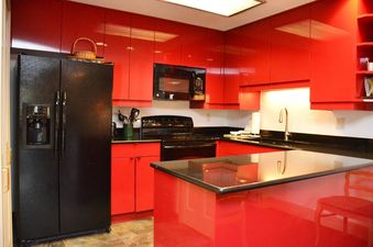 A red kitchen with black appliances, a black granite countertop, and a red island.