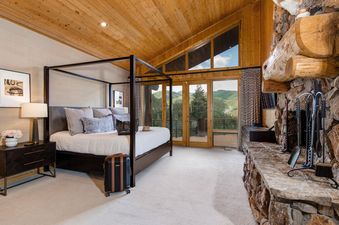 A luxurious master bedroom with a four-poster bed, a stone fireplace, and floor-to-ceiling windows offering mountain views.